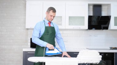 Kravatlı ve önlüklü yakışıklı bir adam çarşaf ütülüyor. temizlik kavramı