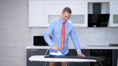 handsome man in tie ironing pants . the kitchen of his house