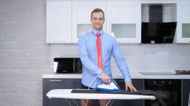 handsome man in tie ironing pants . the kitchen of his house