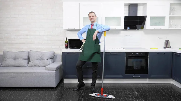 Hombre guapo en corbata y delantal trapea el suelo en la cocina —  Fotos de Stock