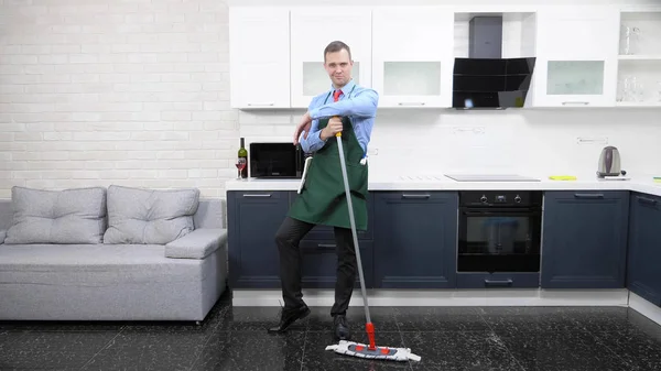 Przystojny mężczyzna w krawacie i fartuch myje podłogę w kuchni — Zdjęcie stockowe