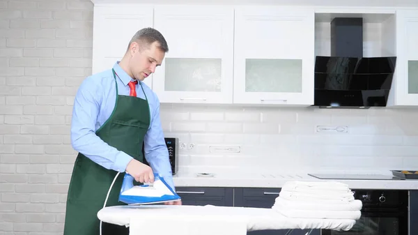 handsome man in a tie and apron ironing linen. cleaning concept