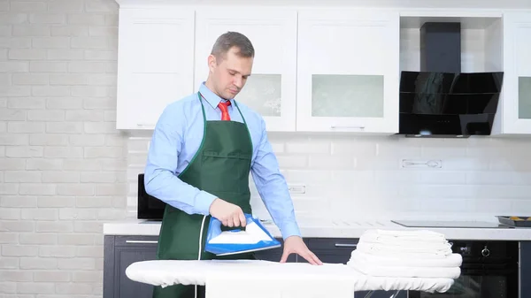 Un hombre guapo con corbata y delantal planchando ropa. concepto de limpieza —  Fotos de Stock