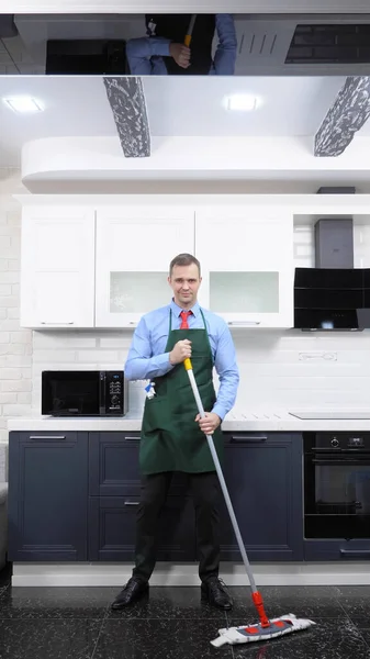 Imagen vertical. hombre guapo en corbata y delantal trapea el suelo en la cocina —  Fotos de Stock