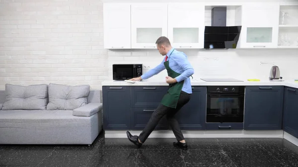 Schöner Mann in Schürze und Krawatte. Reinigung der Küche in der Wohnung — Stockfoto