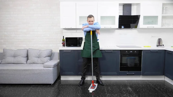 Hombre guapo en corbata y delantal trapea el suelo en la cocina — Foto de Stock