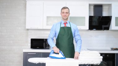 Kravatlı ve önlüklü yakışıklı bir adam çarşaf ütülüyor. temizlik kavramı