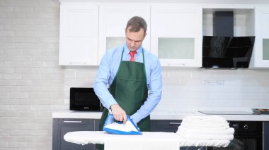 Kravatlı ve önlüklü yakışıklı bir adam çarşaf ütülüyor. temizlik kavramı