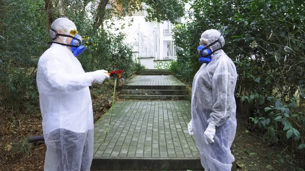 Man and woman in hazmat suits and respirator in the Park. the man gives a flower — Stock Photo, Image