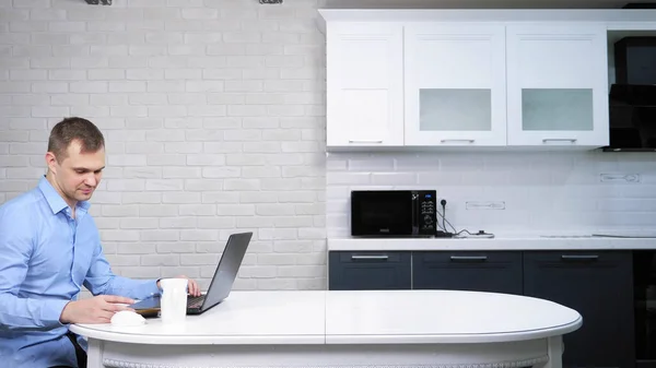 Zakenman met behulp van zijn laptop terwijl zitten aan de tafel in de keuken — Stockfoto