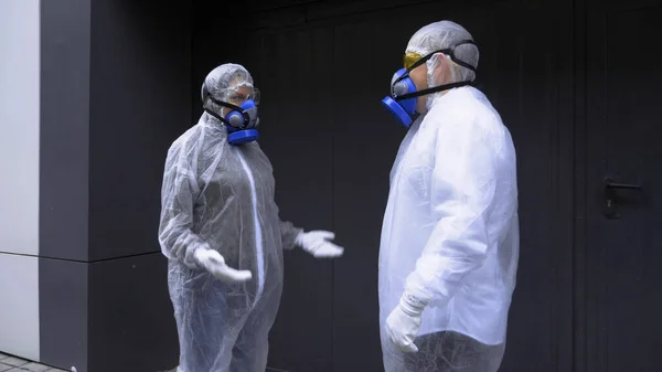 Personas en trajes de protección hablando en la calle frente a una enorme puerta — Foto de Stock