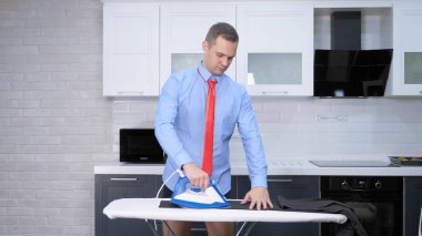 handsome man in tie ironing pants . the kitchen of his house