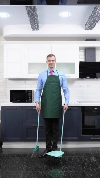 Una imagen vertical. hombre guapo en corbata y delantal barrer el piso de la cocina —  Fotos de Stock