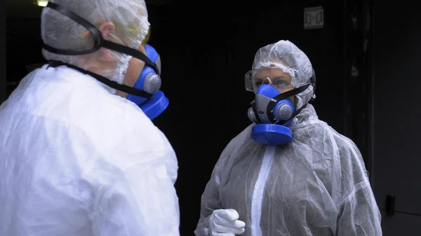 Menschen in Schutzanzügen unterhalten sich auf der Straße vor einem riesigen Tor — Stockfoto