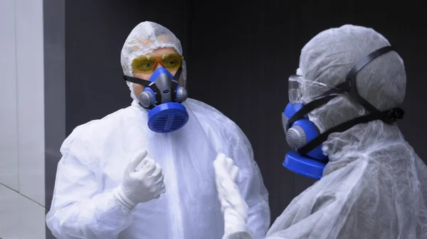 people in protective suits talking on the street in front of a huge gate