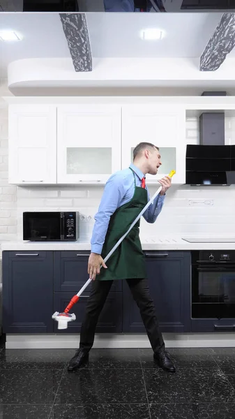Függőleges kép. jóképű férfi nyakkendőben és kötény felmossa a padlót a konyhában — Stock Fotó