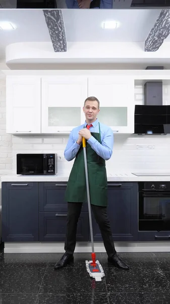 Вертикальне зображення. красивий чоловік в краватці і фартух мацає підлогу на кухні — стокове фото