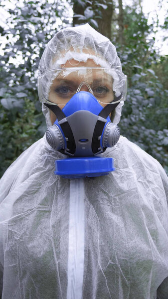 vertical. Portrait of a woman in a protective suit and a respirator on nature