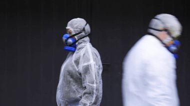 Bulanık insanlar koruyucu giysiler ve solunum cihazlarıyla teknolojik binaların önünden geçiyor