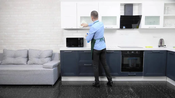 Um homem bonito de avental e gravata. limpa a cozinha no apartamento — Fotografia de Stock