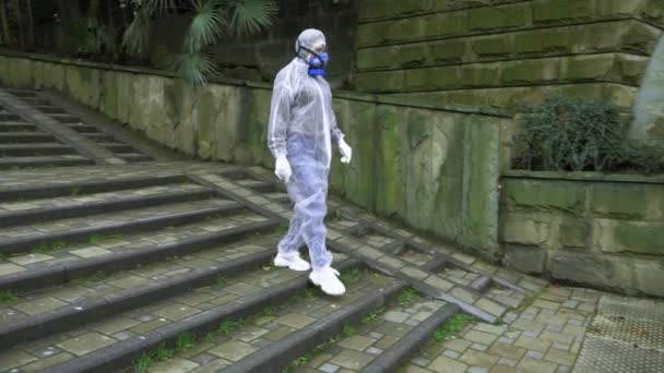 A man and a woman in protective suits and respirators, go to the Park — Stock Video