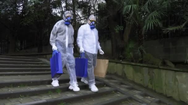 A man and a woman in protective suits and respirators, go to the Park — Stock Video