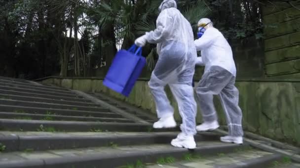 A man and a woman in protective suits and respirators, go to the Park — Stock Video