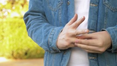 Elleri yakın çekim. Adam alyansını çıkarıp sokakta dikiliyor..