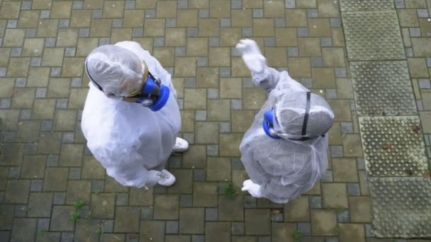 Ein Mann und eine Frau in Schutzanzügen und Atemschutzmasken gehen in den Park — Stockvideo
