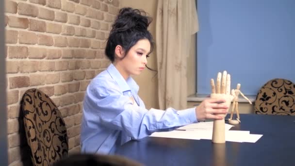 Красивая брюнетка рисует эскиз с деревянным манекеном — стоковое видео