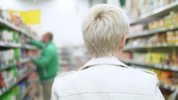 Beautiful stylish woman in the store between the shelves chooses products — Stock Video