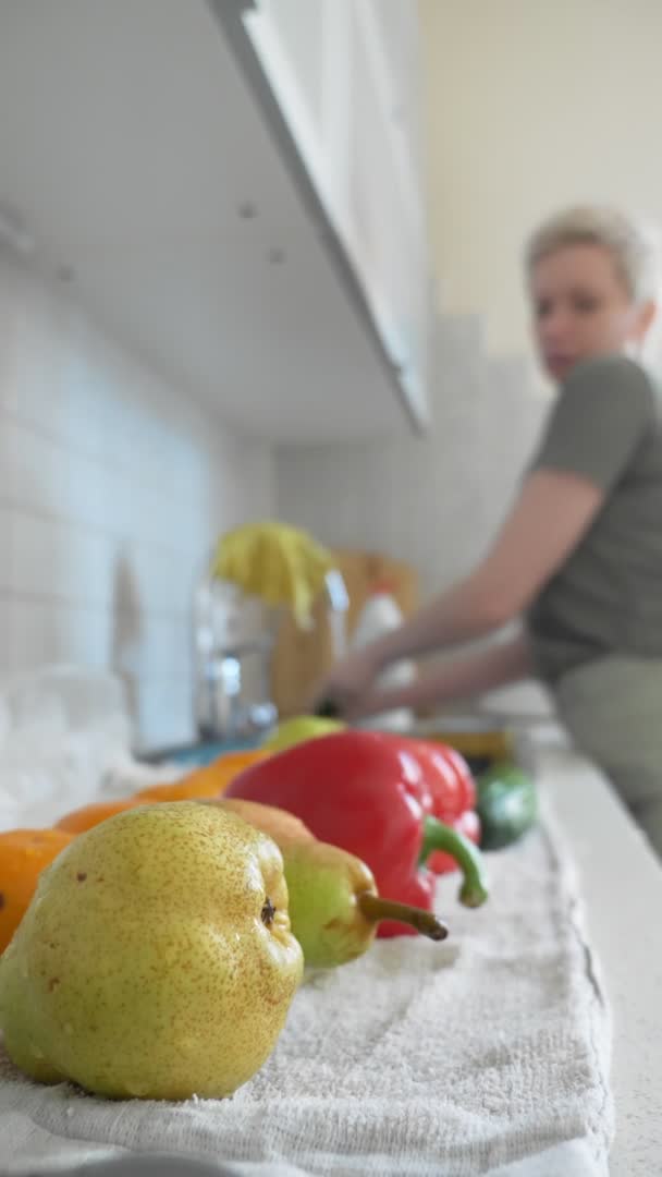 Tiro vertical, una mujer lava verduras y frutas en la cocina en casa . — Vídeo de stock