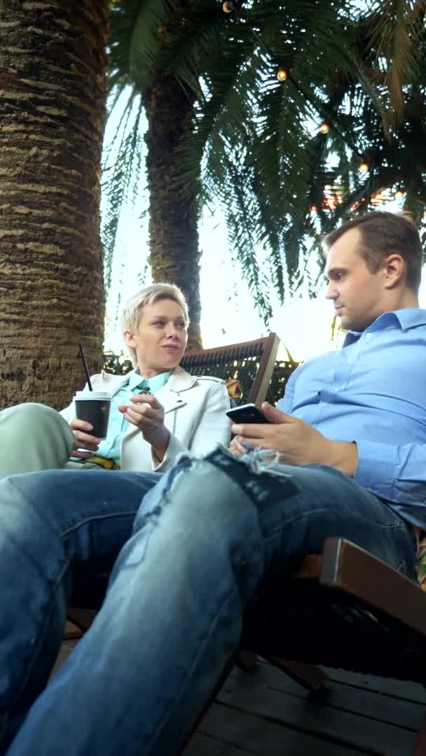 Verticalement. couple homme et femme boire du café dans le café sous les palmiers — Video