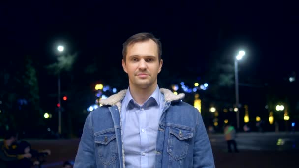 Schöner Mann in der Jacke auf einer Straße in der Stadt bei Nacht, der in die Kamera schaut — Stockvideo