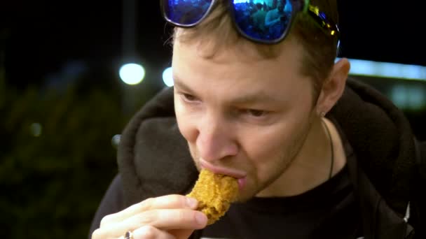 Fechar. homem comendo asas de frango sentado em um café fora à noite — Vídeo de Stock