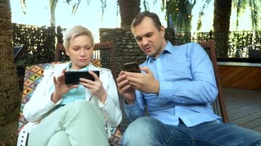 Çift erkek ve kadın açık bir kafede otururken akıllı telefonlarını kullanıyor.