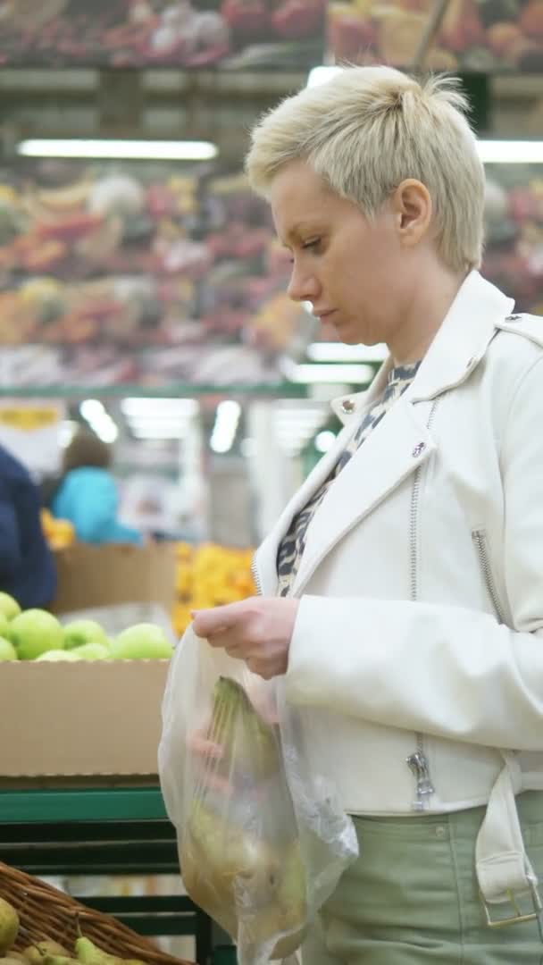 Κάθετη βολή. μια γυναίκα επιλέγει αχλάδια στο σούπερ μάρκετ — Αρχείο Βίντεο