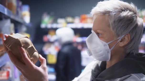 Mujer rubia de pelo corto con máscara médica en la tienda de comestibles. pandemia — Vídeo de stock