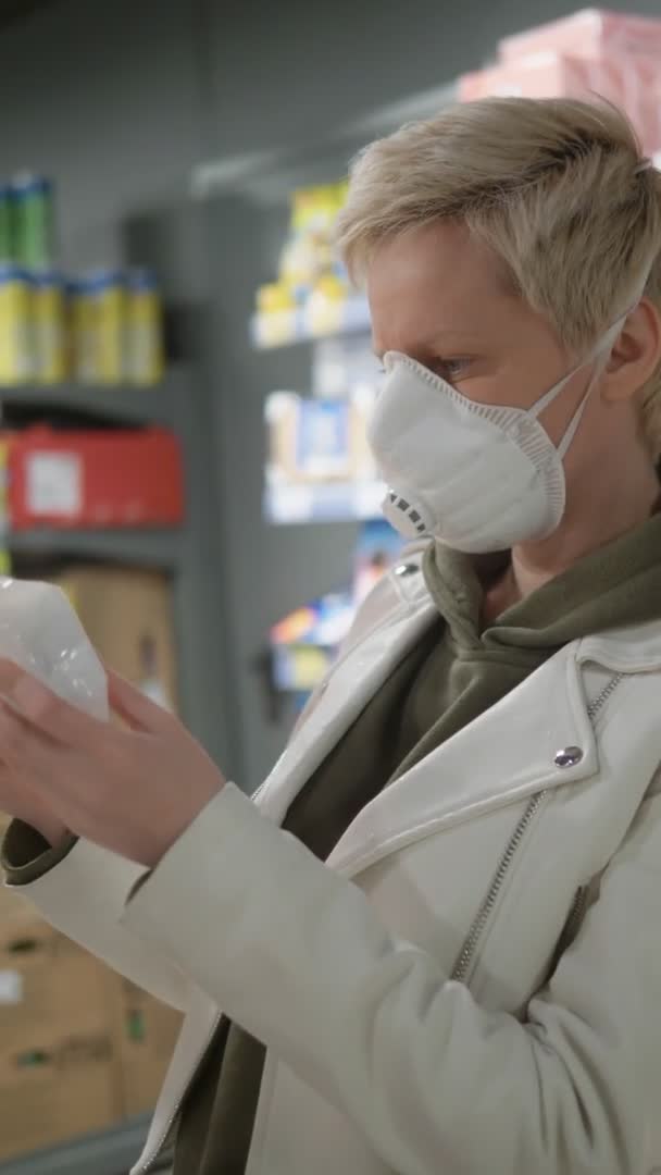 Вертикальный выстрел. Блондинка в медицинской маске в продуктовом магазине. пандемия — стоковое видео