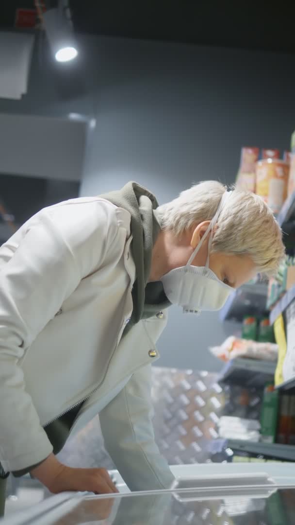 Вертикальний постріл. блондинка в медичній масці в продуктовому магазині. пандемія — стокове відео