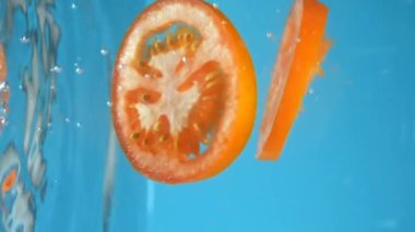 Dikey çekim. Doğranmış domatesler suya düşer. mavi pişirme arkaplanı