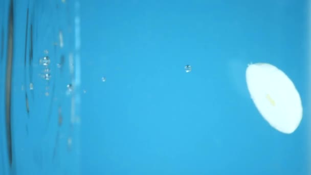 Vertikalt. Hackade lökringar faller ner i vattnet. blå bakgrund. — Stockvideo