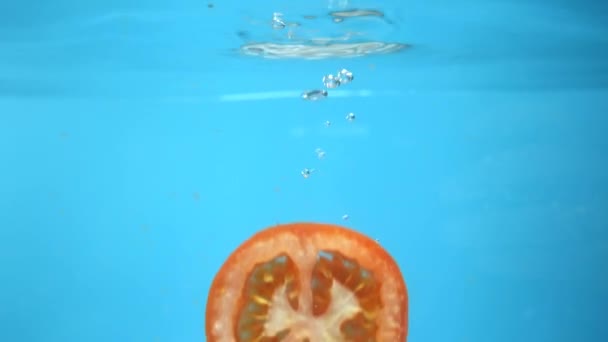Подрібнені помідори потрапляють у воду. синій кухонний фон — стокове відео
