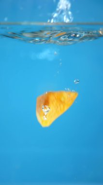 Dikey. Doğranmış havuç suya düşer. mavi arkaplan.