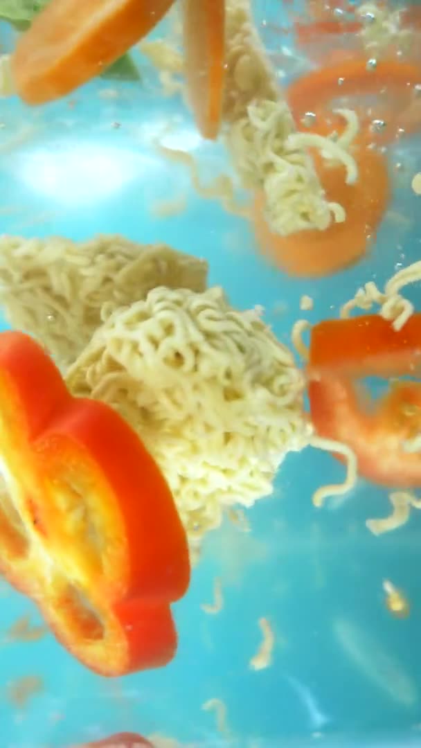 Vertical. légumes hachés et nouilles instantanées tombent dans l'eau . — Video