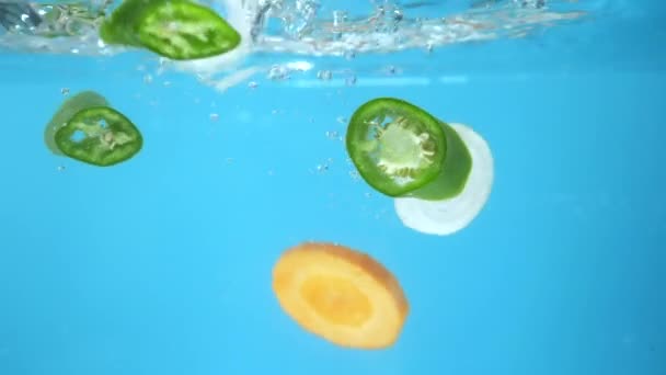 Нарезанные овощи падают в воду. голубой фон. приготовление пищи — стоковое видео