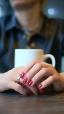 Dikey çekim. Yakın plan. Kadın bir kafede otururken alyansını çıkarıyor.