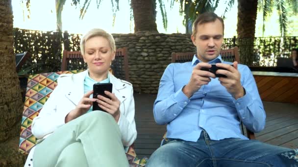 Paar man en vrouw gebruik maken van hun smartphones zitten in een cafe outdoor — Stockvideo