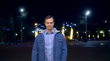 Geceleri şehir sokaklarında ceketli yakışıklı bir adam kameraya bakıyor.