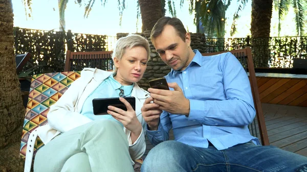 Pareja de hombres y mujeres utilizan sus teléfonos inteligentes sentados en un café al aire libre —  Fotos de Stock